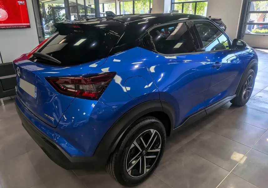 Nissan Juke Hybrid 2025 en bleu magnétique avec toit noir, vue 3/4 arrière droit en intérieur showroom.