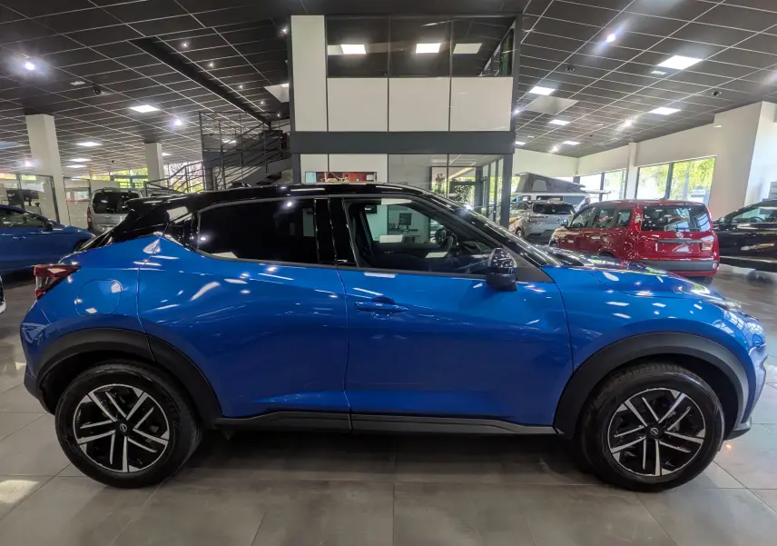 Vue de profil côté gauche du Nissan Juke Hybrid 2025 en bleu magnétique avec toit noir et jantes noires à motifs.