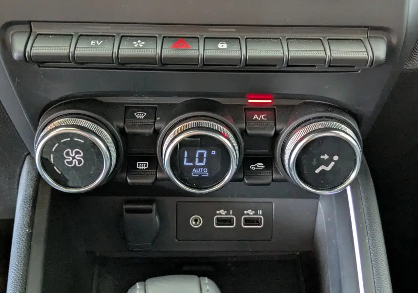 Gros plan sur les commandes de climatisation et connectiques USB de la Renault Clio hybride 2025 en intérieur noir.