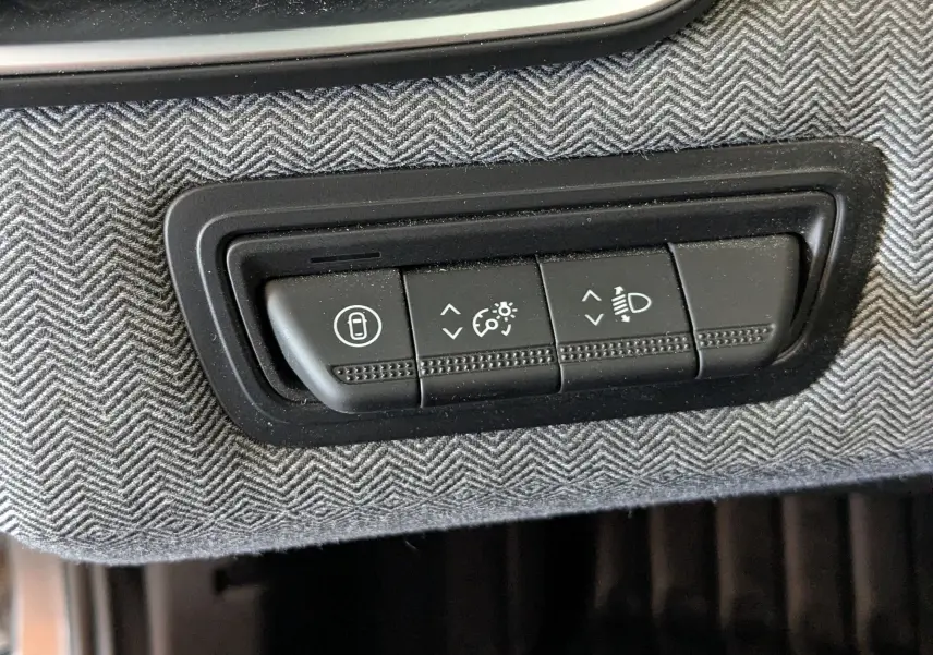 Gros plan sur les commandes d’éclairage et verrouillage intégrées dans le revêtement gris à motif chevrons de la Renault Clio hybride 2025.