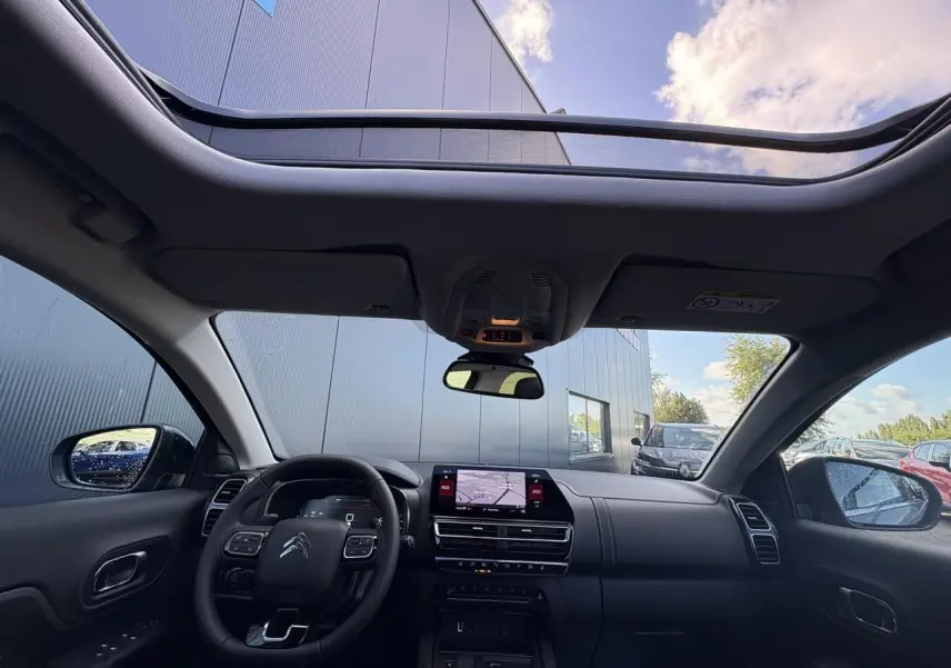 Vue intérieure avant du Citroën C5 Aircross 2025 avec toit panoramique et tableau de bord noir moderne.