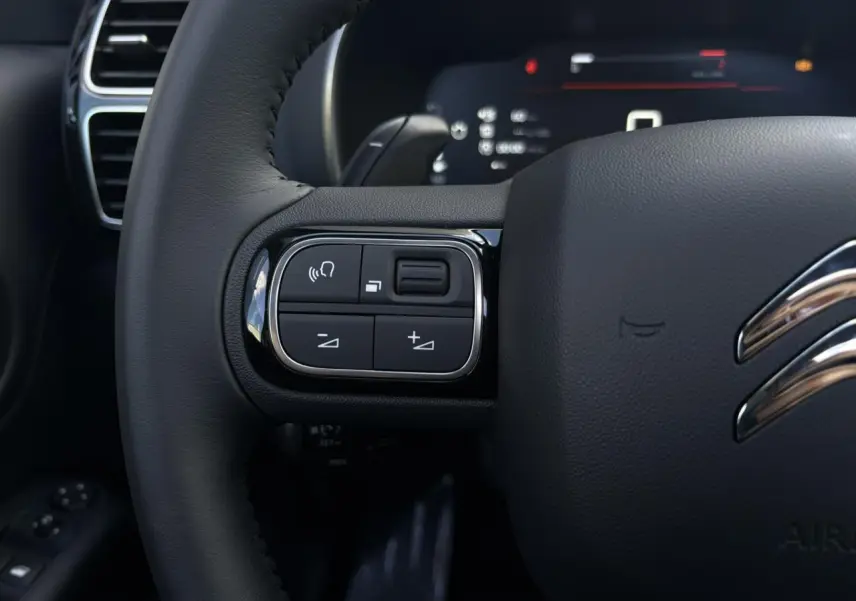 Gros plan sur les commandes gauche du volant cuir noir du Citroën C5 Aircross 2025, avec logo chrome visible.