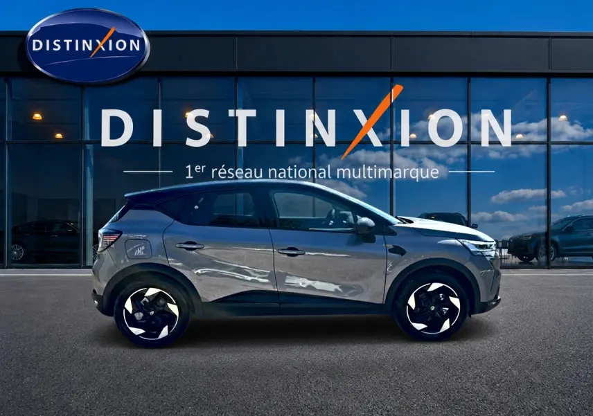 Profil droit d’un Renault Captur gris cassiopée 2026 devant une vitrine Distinxion, avec jantes alu noires et blanches.