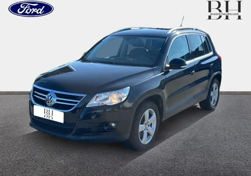 Volkswagen Tiguan noir en 3/4 avant droit, avec jantes alu et phares allumés sur fond neutre.