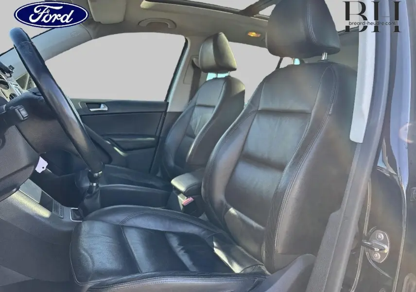 Vue intérieure côté gauche montrant les sièges avant sport en cuir noir et le volant multifonction d’un Volkswagen Tiguan beige.