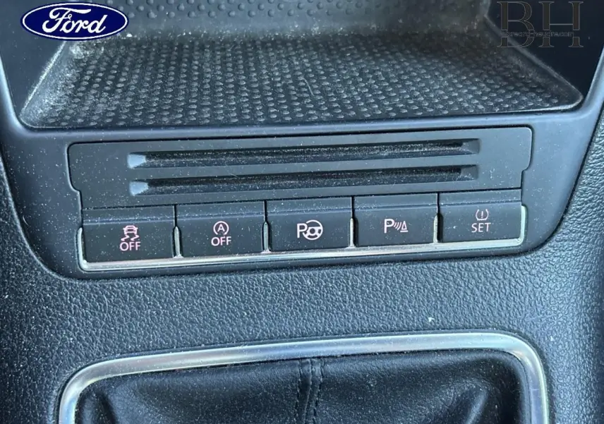 Gros plan sur la console centrale d’un Volkswagen Tiguan beige, montrant les boutons de contrôle et le soufflet de levier de vitesse en cuir noir.