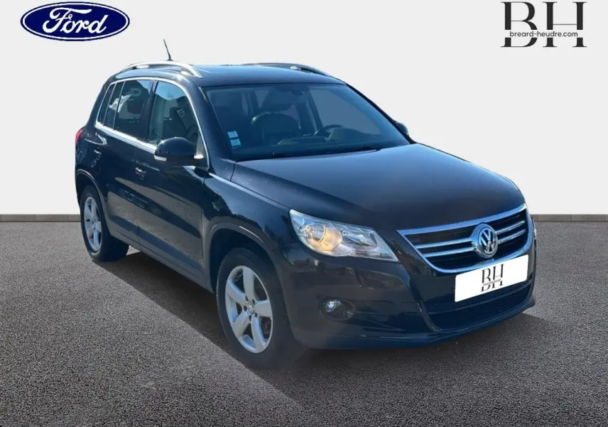 Volkswagen Tiguan noir en 3/4 avant droit, avec jantes alu et phares allumés sur fond clair.