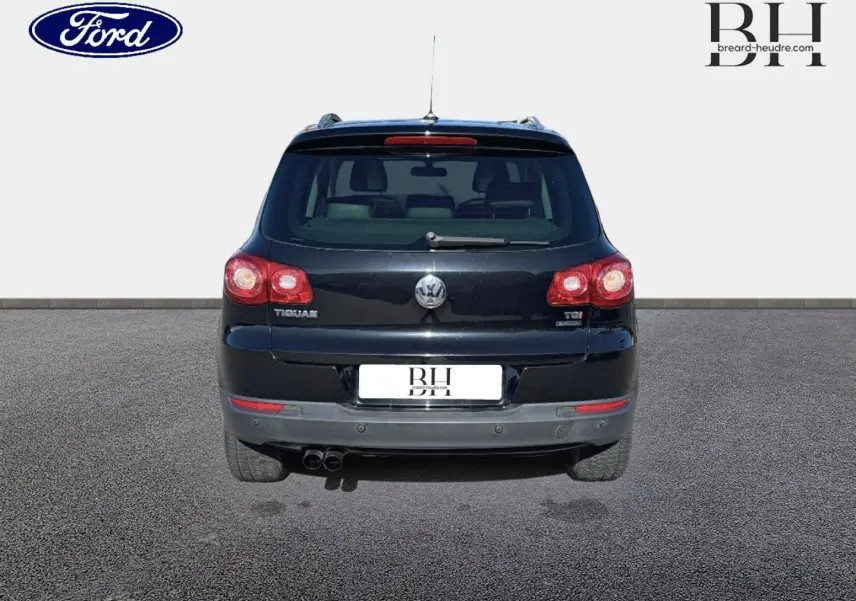 Vue arrière d'un Volkswagen Tiguan noir, avec feux arrière allumés et double sortie d'échappement visible.