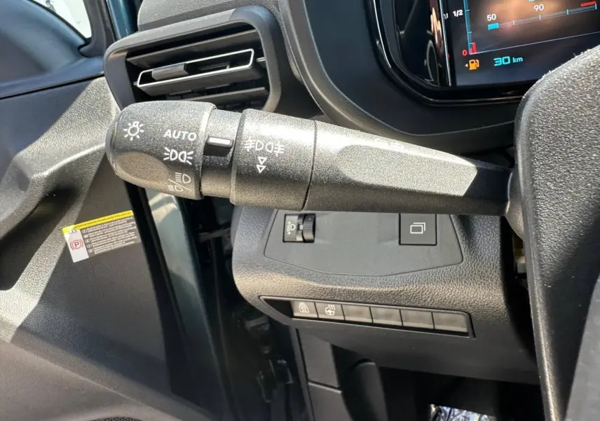 Gros plan sur la commande des phares à gauche du volant dans l’habitacle noir du Citroën Berlingo Kiama Blue.