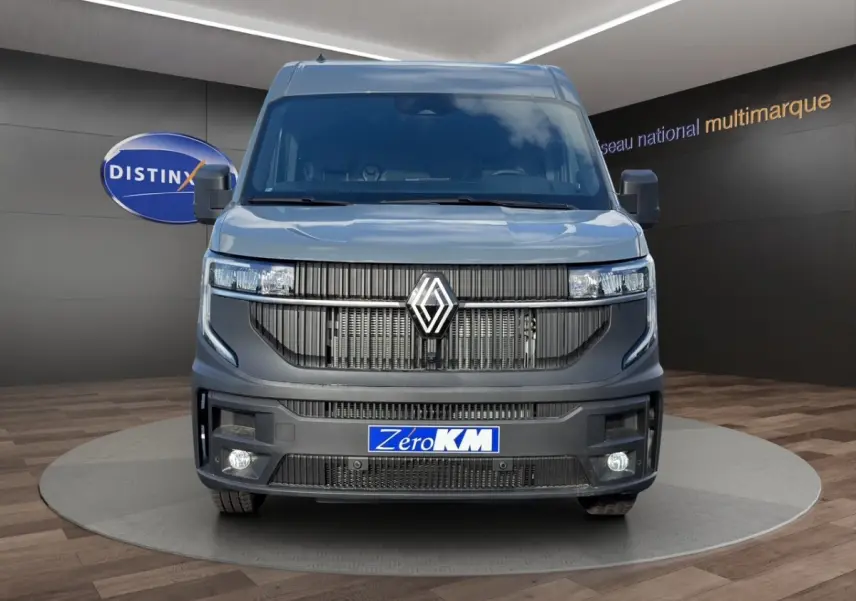 Vue avant d’un Renault Master gris avec calandre noire et feux LED, sur fond intérieur showroom multimarque.