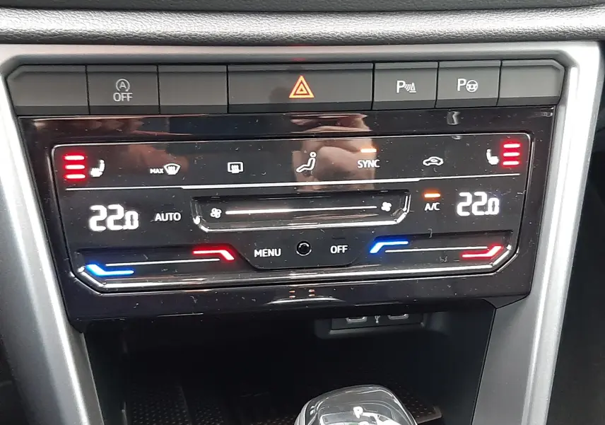 Vue rapprochée du tableau de bord et de la console centrale du Volkswagen T-Roc 1.5 TSI gris, avec commandes de climatisation digitales et levier de boîte auto.