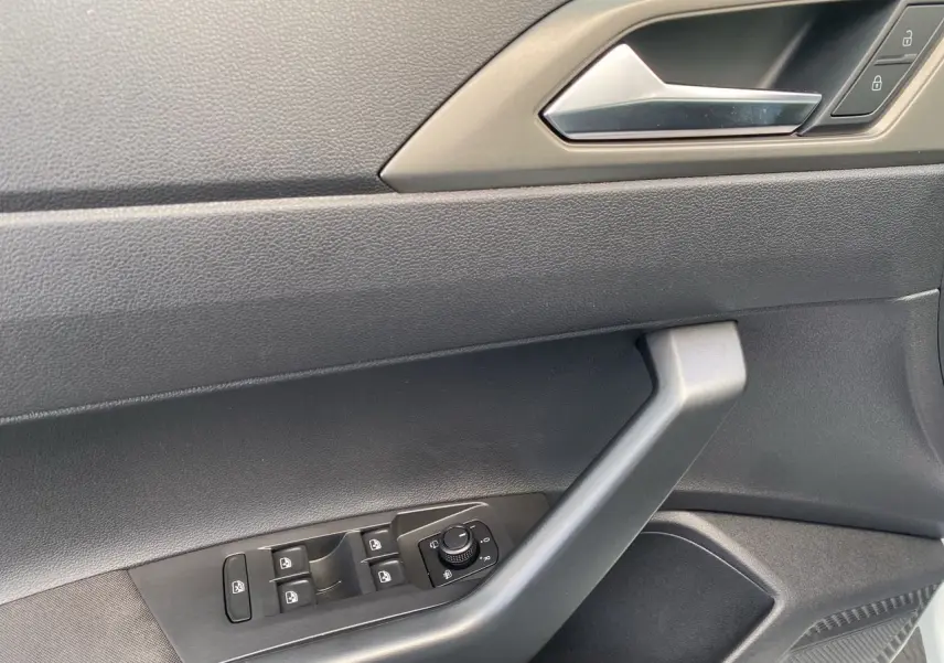 Gros plan sur la porte côté conducteur de la Volkswagen Polo blanche, montrant les commandes électriques des vitres et le bouton de réglage des rétroviseurs.
