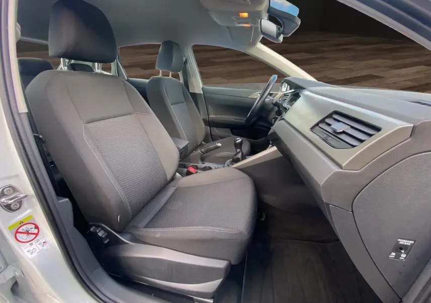 Vue intérieure côté droit de la Volkswagen Polo blanche, montrant les sièges avant en tissu noir et la console centrale.