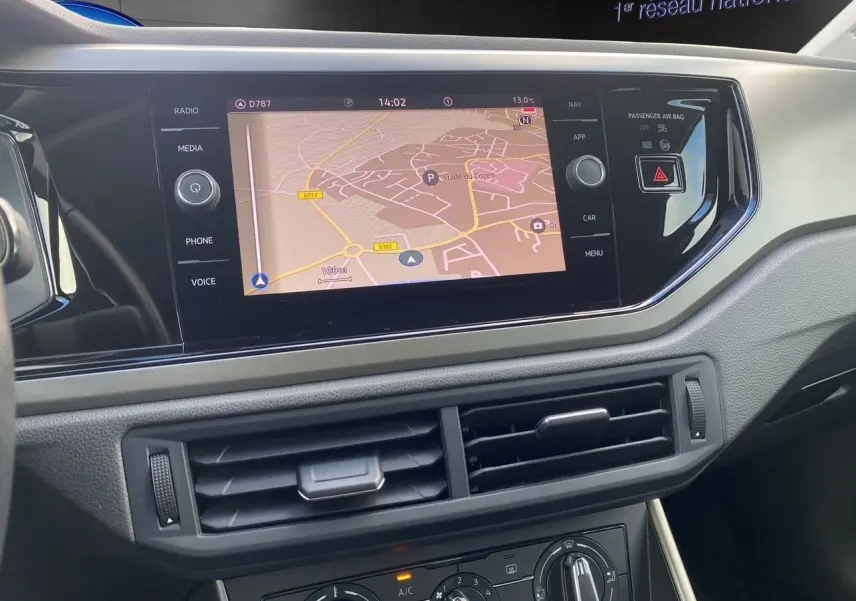 Vue rapprochée de l’écran tactile central avec navigation et commandes de climatisation d’une Volkswagen Polo blanche.
