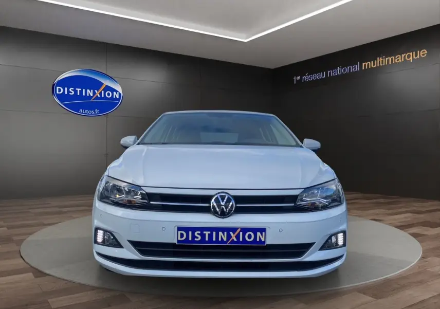 Volkswagen Polo blanc pure vue de face en intérieur, avec phares et feux diurnes allumés.