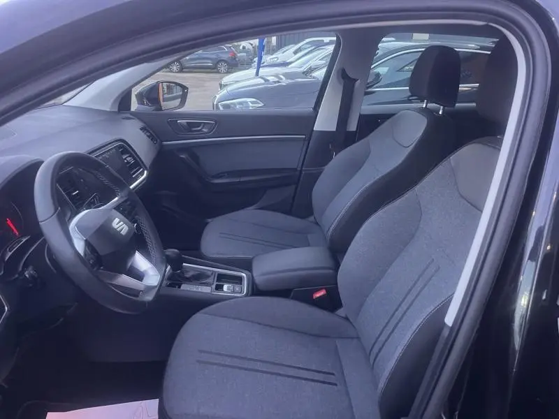 Vue intérieure côté conducteur du SEAT Ateca noir, montrant les sièges tissu gris, volant cuir multifonction et console centrale.