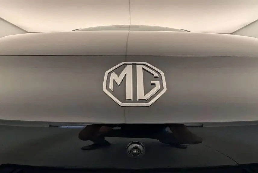 Gros plan sur le logo MG en relief sur la malle arrière Pebble Black, avec caméra de recul visible en dessous.