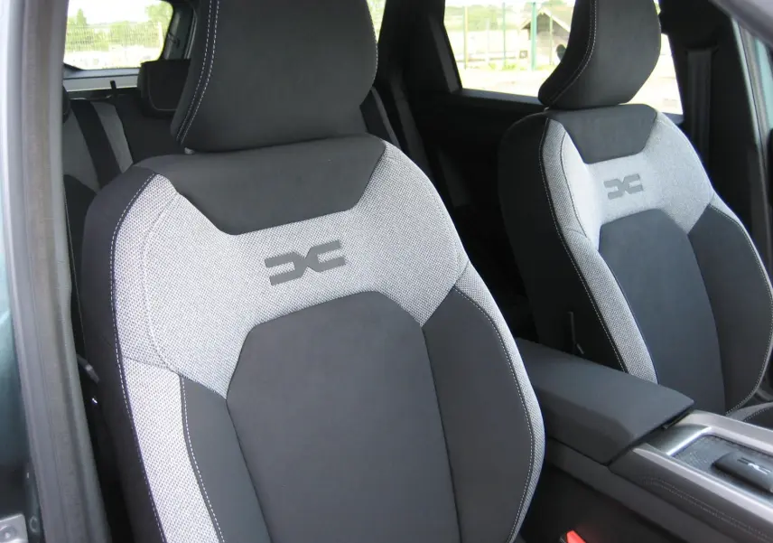 Gros plan sur les sièges avant gris clair et noir du Dacia Bigster 1.8 Hybrid 155 CH, avec logo distinctif brodé.