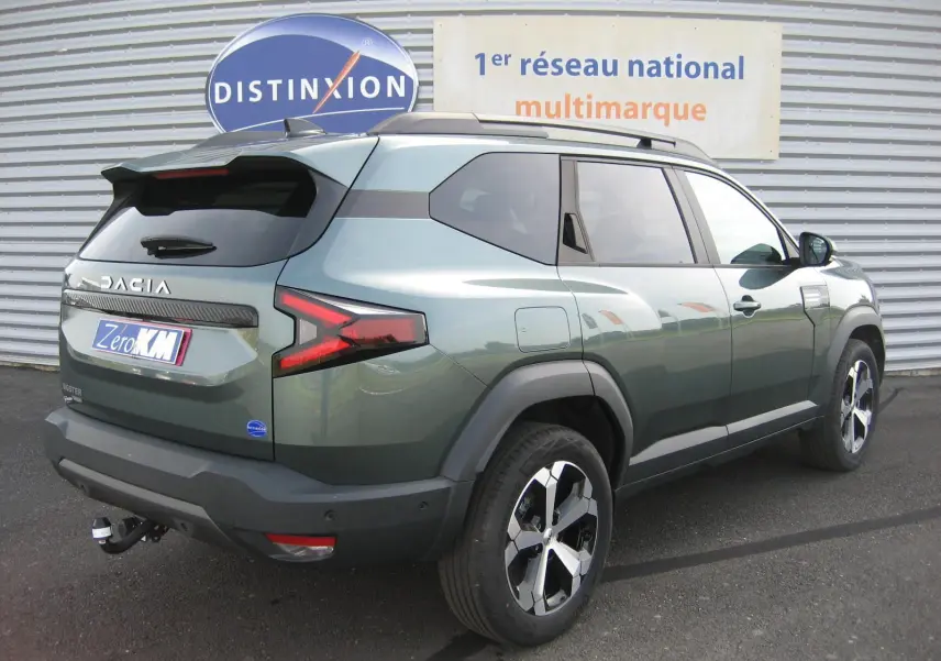 Vue 3/4 arrière droite du Dacia Bigster gris schiste avec barres de toit et jantes alliage noires et argentées.