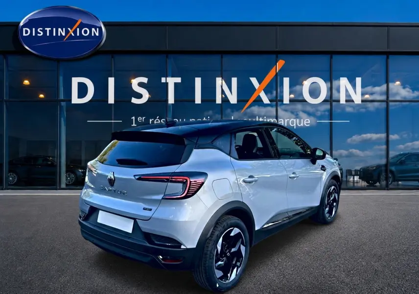 Vue 3/4 arrière droite du Renault Captur gris rafale avec toit noir et jantes alu noires devant une vitrine Distinxion.