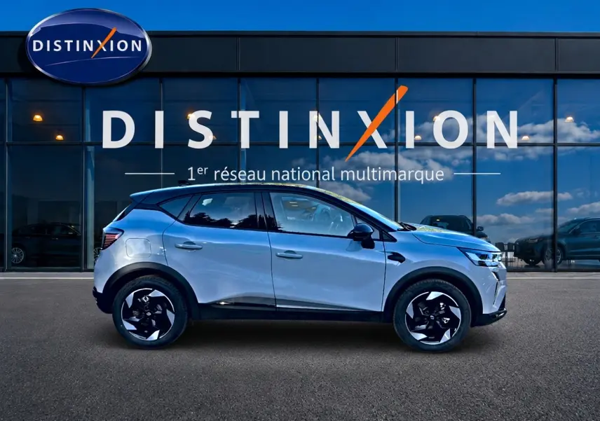 Renault Captur 1.8 e-tech hybride gris rafale en profil droit devant vitrine Distinxion, jantes noires et blanches.