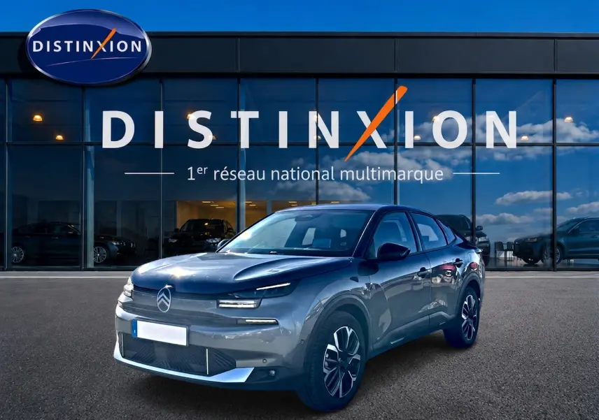 Vue 3/4 avant d'une Citroën C4 X gris mercure garée devant une vitrine avec logo Distinxion.