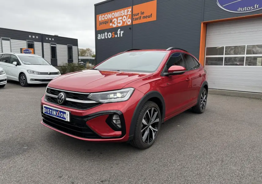Volkswagen Taigo Rouge Roi en 3/4 avant droit, jantes noires brillantes, feux LED allumés, devant un garage autos.fr.