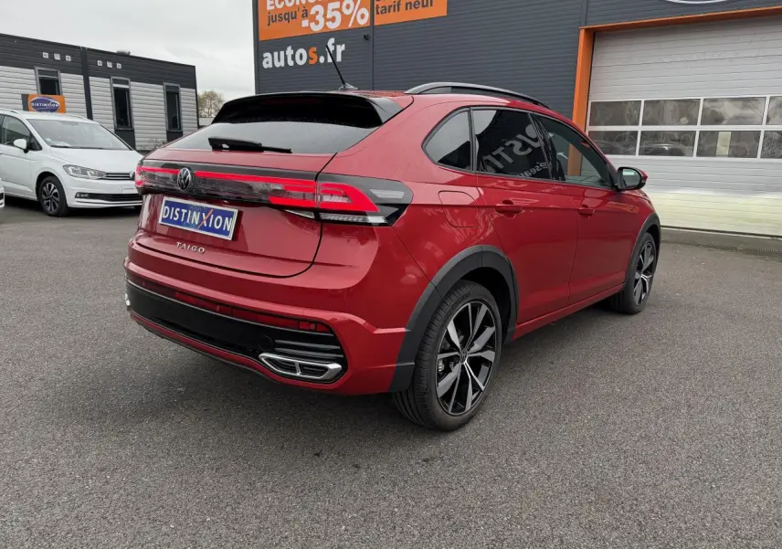 Vue 3/4 arrière droite d'un Volkswagen Taigo Rouge Roi avec jantes noires brillantes et feux arrière LED allongés.