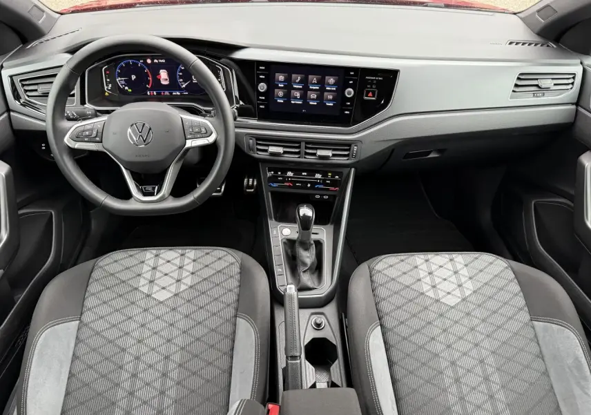 Vue intérieure avant du Volkswagen Taigo 2025, tableau de bord moderne avec écran tactile et sièges tissu gris à motifs géométriques.