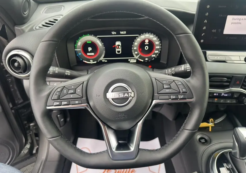 Vue intérieure centrée sur le volant cuir du Nissan Juke 2025 gris squale, avec tableau de bord digital et commandes intégrées.