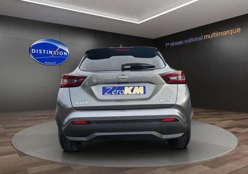 Vue arrière d'un Nissan Juke 2025 gris squale hybride, avec feux arrière LED et logo distinctif sur un podium intérieur.