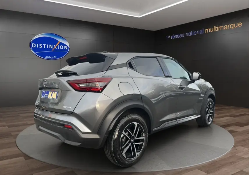 Nissan Juke 2025 gris squale en 3/4 arrière droit, avec jantes noires et détails hybrides visibles sur le hayon.