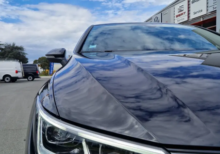 Gros plan sur le phare avant gauche d’une Volkswagen Golf 8 noire intense métal, reflet du ciel sur la carrosserie.