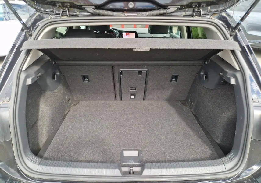 Vue arrière du coffre ouvert d'une Volkswagen Golf 8 noire intense métal, montrant un espace de chargement propre et bien agencé.