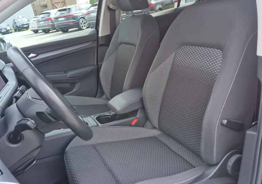 Vue intérieure côté conducteur de la Volkswagen Golf 8 noire, mettant en valeur les sièges tissu gris à motifs et l'habitacle moderne.