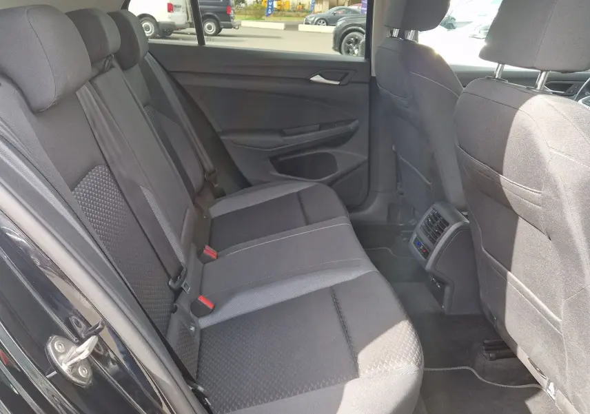 Vue intérieure arrière droite de la Volkswagen Golf 8 noire, montrant les sièges arrière en tissu et les aérations centrales.