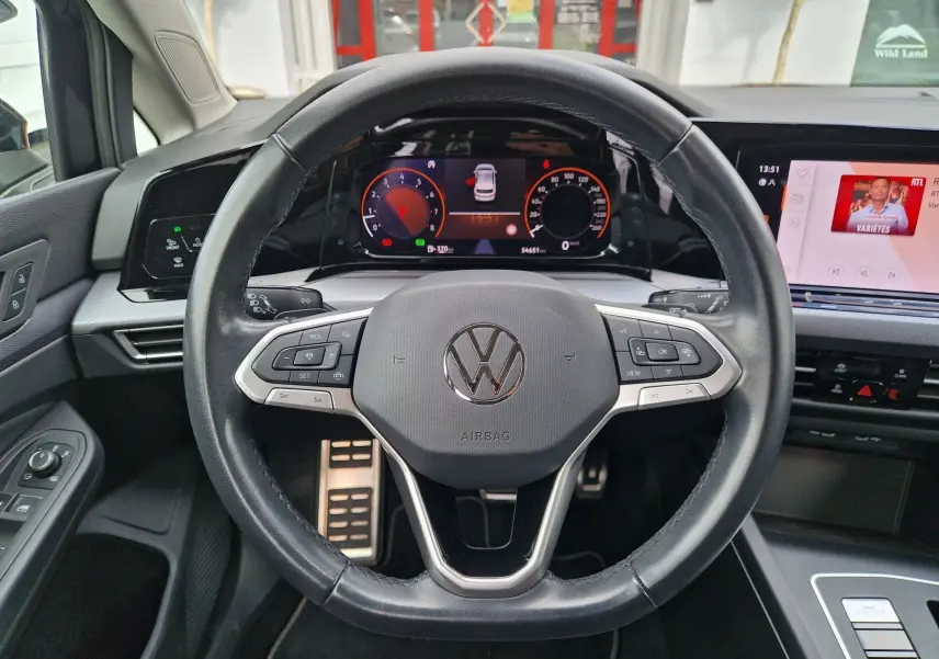 Vue intérieure centrée sur le volant noir de la Volkswagen Golf 8 2023 avec tableau de bord numérique et écran tactile.