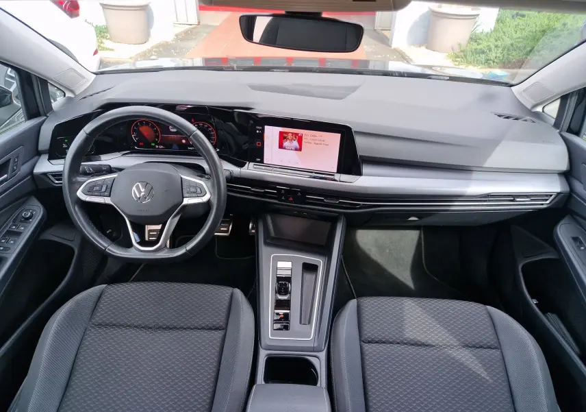 Vue intérieure avant de la Volkswagen Golf 8 noire, mettant en valeur le tableau de bord digital et la console centrale moderne.