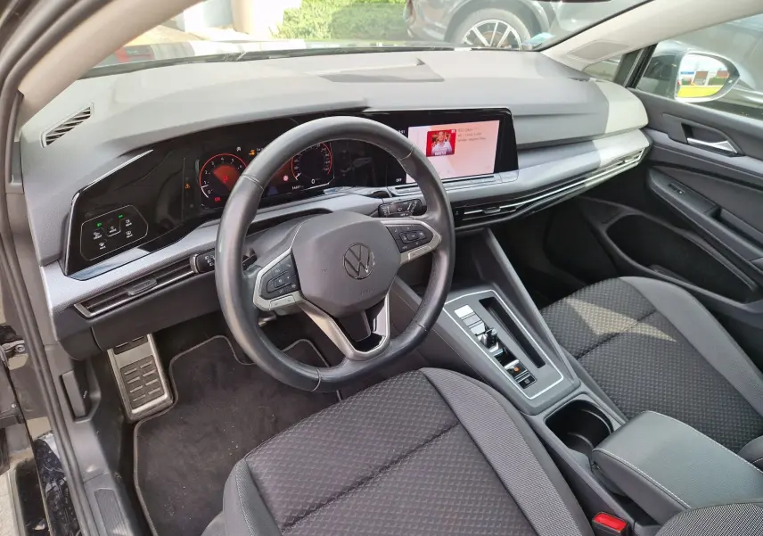 Vue intérieure côté conducteur de la Volkswagen Golf 8 noire, avec tableau de bord digital et écran tactile central.