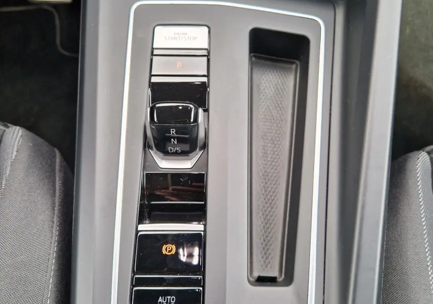 Vue plongeante sur la console centrale noire de la Volkswagen Golf 8, avec levier de vitesses automatique et boutons de contrôle éclairés.