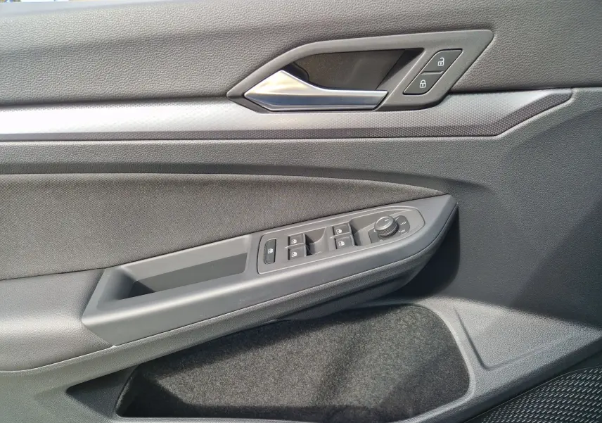 Vue rapprochée de la porte côté gauche de la Volkswagen Golf 8 noire, montrant les commandes des vitres et la poignée intérieure.