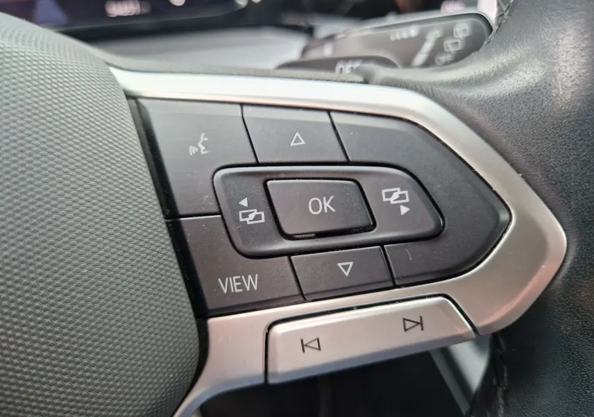 Gros plan sur les commandes multifonctions noires et argent du volant de la Volkswagen Golf 8 noire, côté gauche.