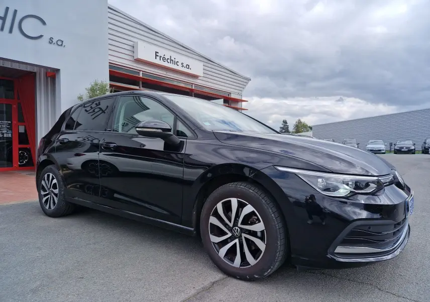 Vue 3/4 avant droite d'une Volkswagen Golf 8 noire intense métal, avec jantes distinctives et phares LED allumés.