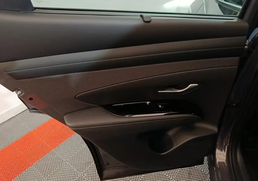Porte arrière droite ouverte du Hyundai Tucson gris foncé, montrant le panneau intérieur en cuir et tissu avec poignée argentée.