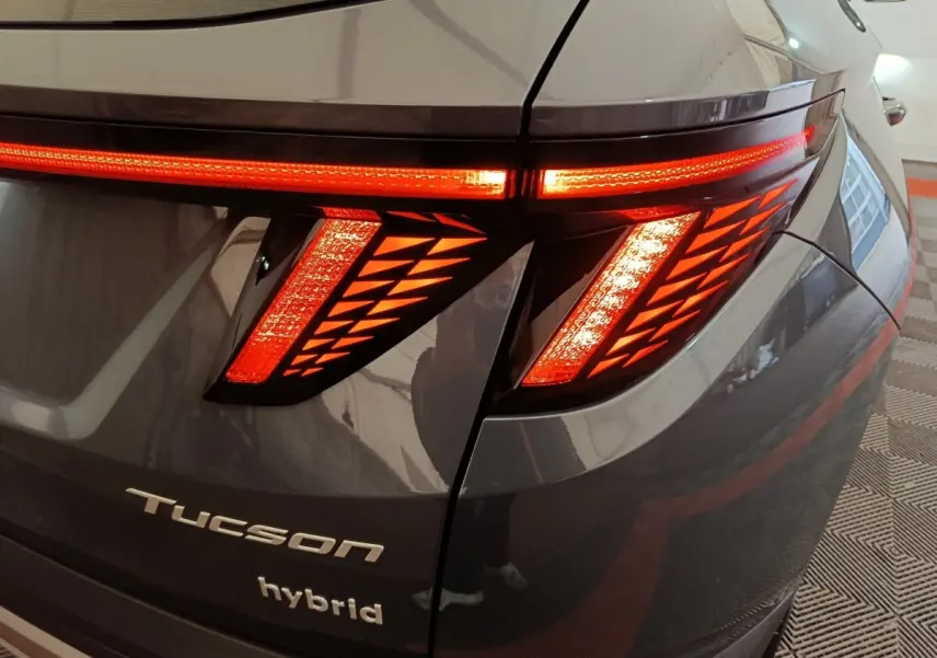 Gros plan sur le feu arrière droit allumé d’un Hyundai Tucson gris foncé hybride avec logo et inscription "hybrid" visibles.