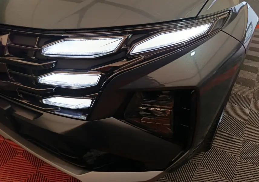 Gros plan sur l'avant droit gris foncé du Hyundai Tucson 2025, mettant en valeur ses feux LED distinctifs et la calandre noire.