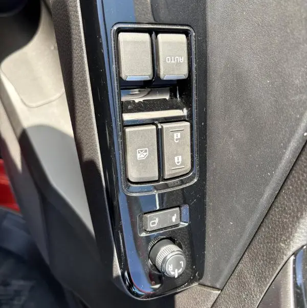 Gros plan sur les commandes des vitres et des rétroviseurs côté conducteur d'un Isuzu D-MAX orange 2026.