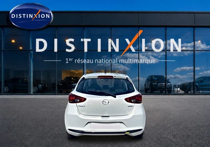 Vue arrière d'une Mazda2 blanche 2024 garée devant une vitrine avec logo Distinxion en arrière-plan.