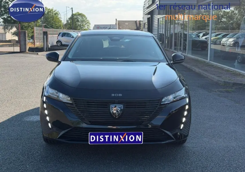 Vue avant d'une Peugeot 308 e-308 noire Perla Nera avec feux LED verticaux allumés sur un parking extérieur.