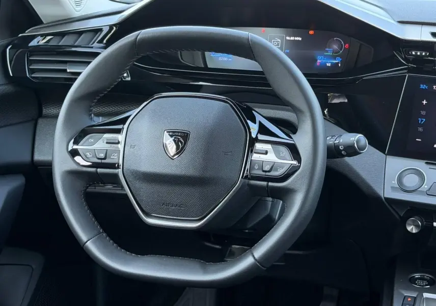 Vue rapprochée du volant multifonction noir et du tableau de bord numérique de la Peugeot e-308 2025.
